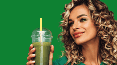 Woman with curly hair and a smug smile looking sideways holding a green smoothie on a green background.